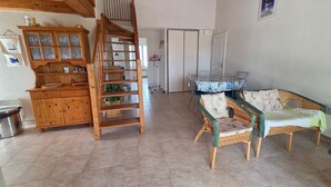 Una escalera de madera, una mesa de comedor con sillas, muebles de mimbre y un aparador con puertas de cristal.