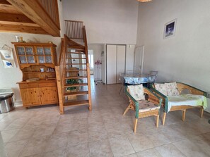 Una escalera de madera, una mesa de comedor con sillas, muebles de mimbre y un aparador con puertas de cristal.