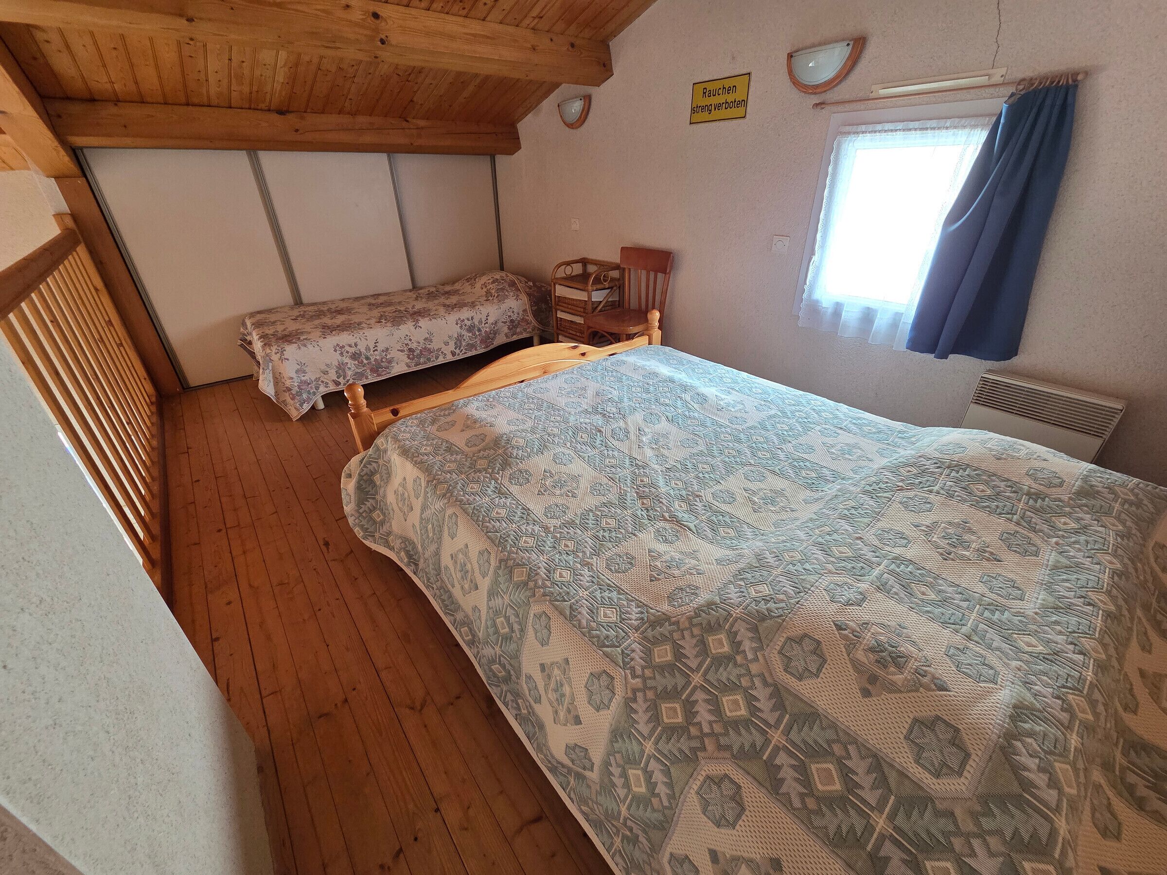 A room with a bed, a chair, a window with curtains, and a sign on the wall.