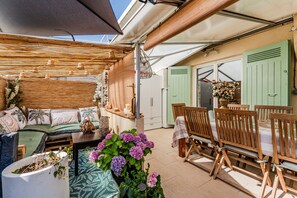 Un patio al aire libre con un sofá, sillas de madera, una mesa y plantas en macetas.