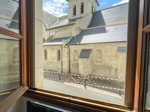 Une vue Ă travers la fenĂȘtre dâun bĂątiment en pierre, dotĂ© de fenĂȘtres en arc de cercle et dâun toit recouvert de tuiles.