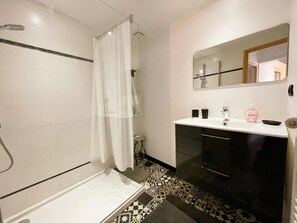 Une salle de bain avec une douche, un lavabo avec un miroir et des carreaux de sol Ă motifs.