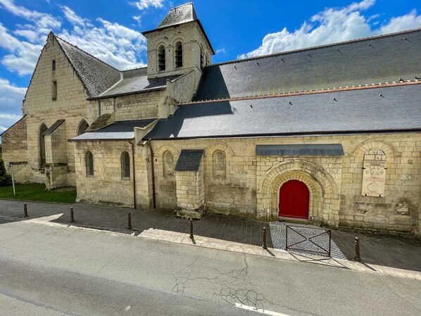 Une église historique en pierre, avec une porte rouge, un clocher et une rue pavée devant.
