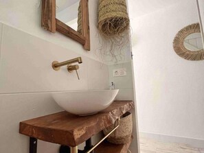 Ein Badezimmer mit einem weißen Aufsatzbecken, einem Holzwaschtisch und einem Spiegel mit einem gewobenen Rahmen.