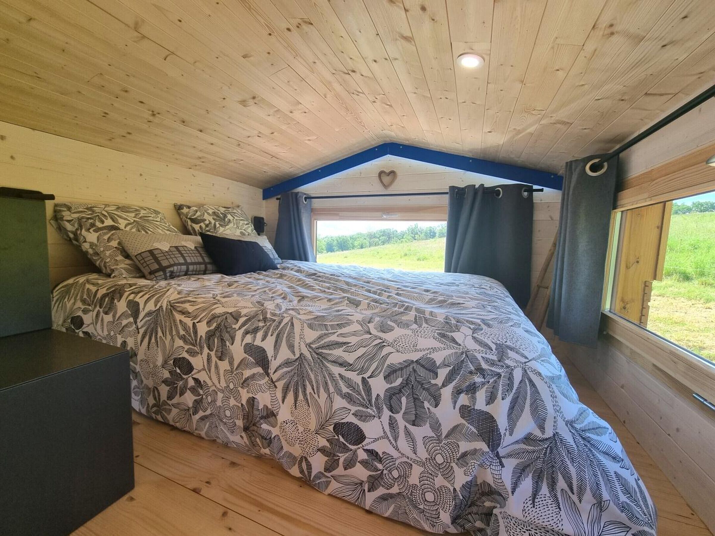 A bedroom with a bed, a dresser, a window with curtains, and a view of the outdoors.