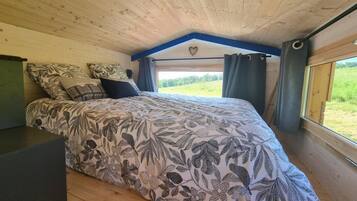 A bedroom with a bed, a dresser, a window with curtains, and a view of the outdoors.