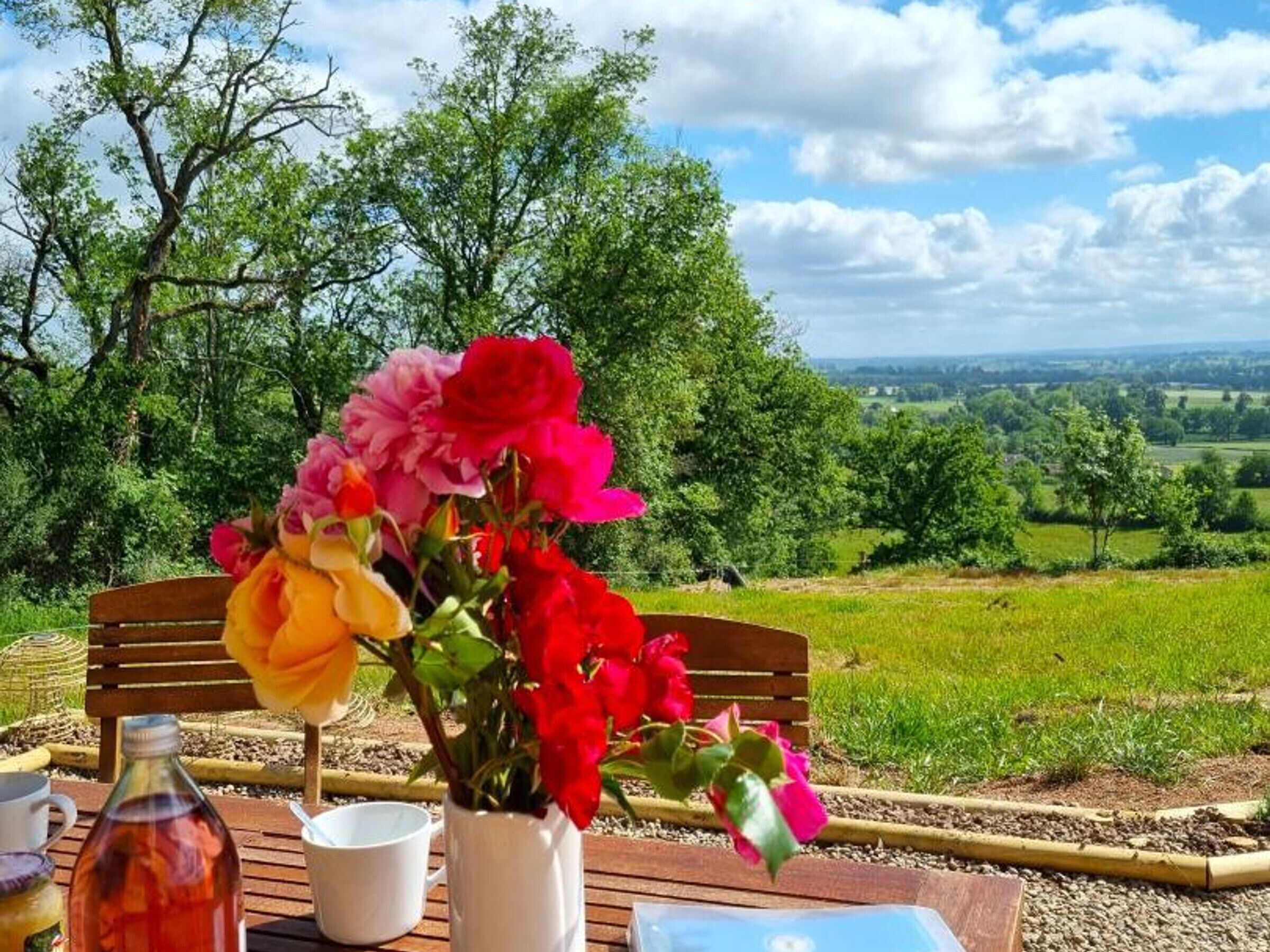 Een houten tafel met een bloemenvaas, een fles en een mok.