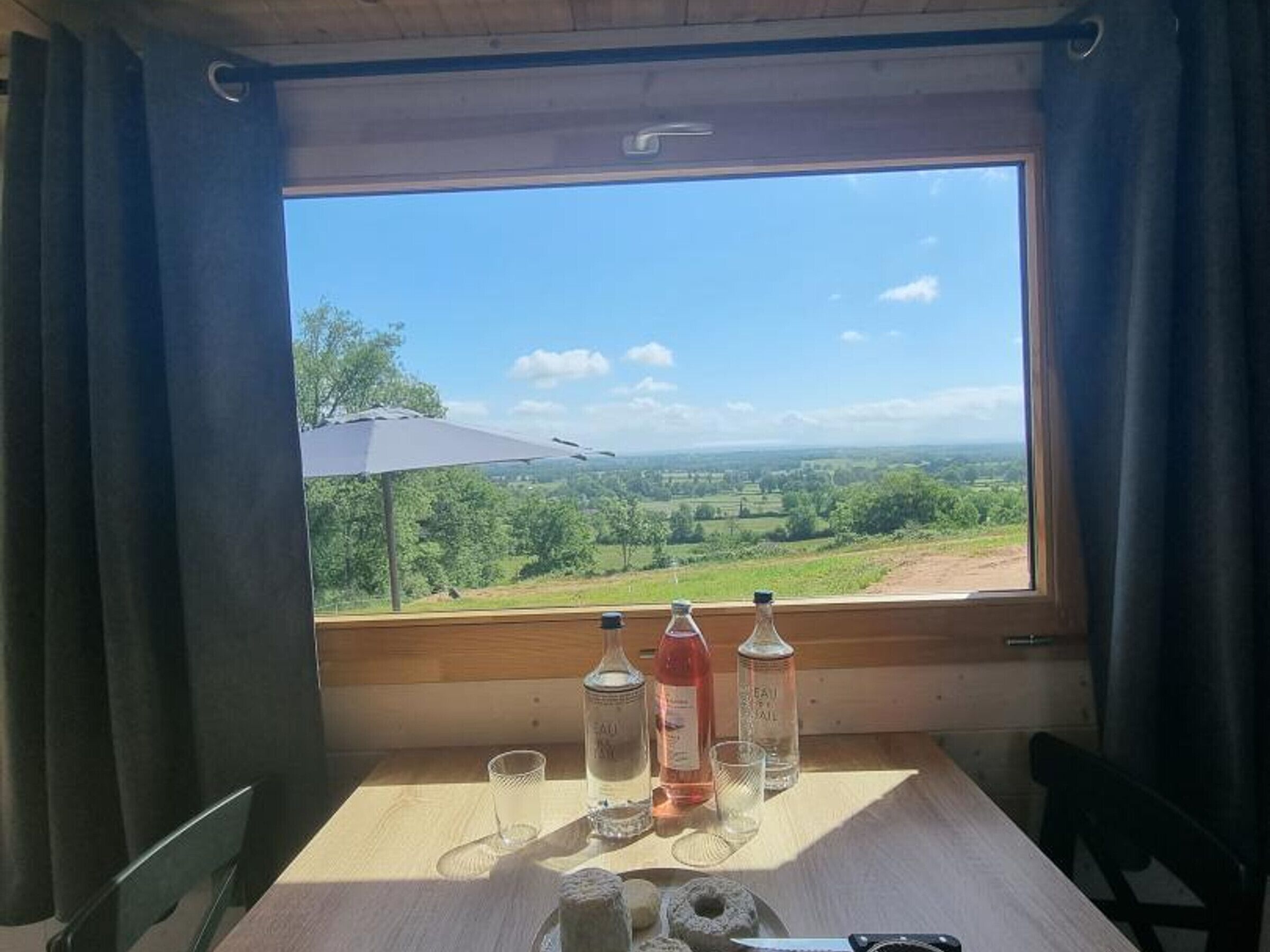 A table with a view of a rural landscape, a bottle of water, a glass, and a knife.