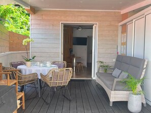 Eine Terrasse im Freien mit Korbmöbeln, einem Esstisch und einem grauen Sofa.
