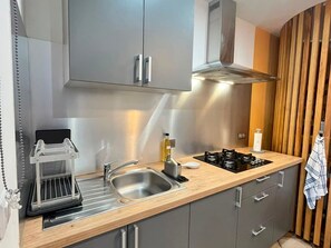 Eine moderne Küche mit grauen Schränken, einer Edelstahl-Spüle, einer eingebauten Dunstabzugshaube und einer Holzausziehtheke.