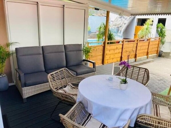 Eine Terrasse mit einer Couch, Korbstühlen und einem runden Tisch.