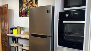 A kitchen with a stainless steel refrigerator, a built-in oven, wooden bar stools, and a wall-mounted microwave. - House with private pool, parking, AC - 4 guests (Saint-Louis)