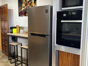 Eine Küche mit einem Edelstahl-Kühlschrank, einem eingebauten Ofen, Holzbarhocker und einer an der Wand befestigten Mikrowelle.