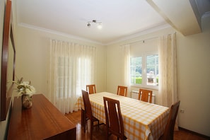Ein Esszimmer mit Tisch für vier Personen, Holzsesseln, einer Blumenvase und einem Fenster mit Vorhängen.