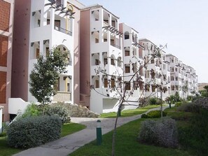 Une rangée d’immeubles résidentiels à plusieurs étages, dotés de balcons, d’un chemin piétonnier pavé et d’espaces verts aménagés.