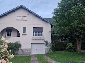 A two-story building with a garage, a small balcony, and a pathway leading to the entrance.