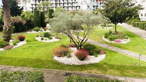 A landscaped garden with a variety of plants and trees, a pathway, and modern buildings in the background. - Air-conditioned apartment in city center - 2 guests (La Grande-Motte)