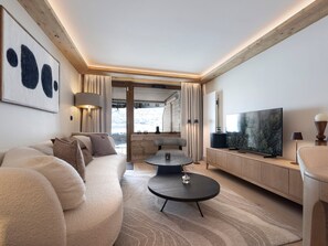 Ein modernes Wohnzimmer mit einer Couch, einem Couchtisch, einem Fernseher und Blick auf eine verschneite Landschaft.