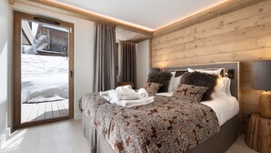 Ein modernes Schlafzimmer mit einem großen Bett, Holzvertäfelung, Blick auf eine verschneite Landschaft und einer zur Außenseite führenden Tür.