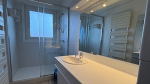 Un baño moderno con ducha de vidrio, un espejo grande y un tocador blanco.