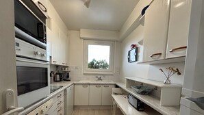 Cocina compacta con lavadora, horno, microondas y ventana.