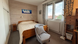 Un dormitorio con una cama de madera, una silla a rayas, una ventana con cortinas y un radiador.