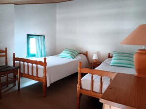 Ein Zimmer mit zwei Holzbett, einem Sessel, einem Tisch, einer Lampe und einem Fenster mit Vorhängen.