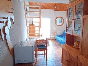 Ein Zimmer mit einem Holzschrank, einem Tisch mit Stuhl, einem blauen Sofa, einer Leiter und einem kleinen Tisch mit Lampe.