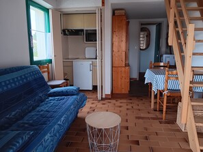 Ein kompakter Wohnraum mit einer Couch, einem kleinen Tisch, einer Küchenzeile und einer Holztreppe.