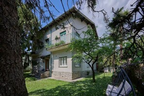 Ein zweistöckiges Haus mit Balkon, einer kleinen Veranda und einem Baum im Garten.