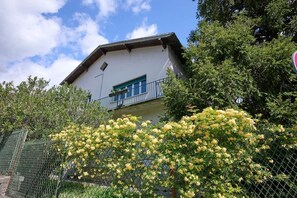 A white building with a balcony, surrounded by greenery and yellow flowering bushes. - The Yellow Roses: Family Room (Mandello del Lario)