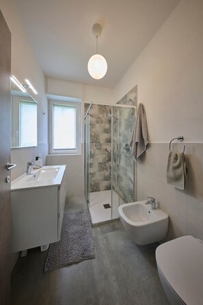 A modern bathroom with a glass shower enclosure, a bidet, and a toilet. - The Yellow Roses: Family Room (Mandello del Lario)