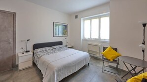 Ein Schlafzimmer mit Bett, Nachttischen, einem Sessel, einem Tisch, einem Fenster und einer Heizung.