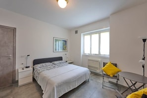 Ein Schlafzimmer mit Bett, Nachttischen, einem Sessel, einem Tisch, einem Fenster und einer Heizung.