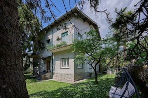 Ein zweistöckiges Haus mit Balkon, einer kleinen Veranda und einem Baum im Garten.