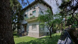Ein zweistöckiges Haus mit Balkon, einer kleinen Veranda und einem Baum im Garten.