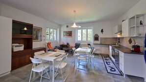 Eine moderne Küche mit weißen Schränken, ein Essbereich mit weißen Stühlen und ein großes Fenster, das für natürliches Licht sorgt.