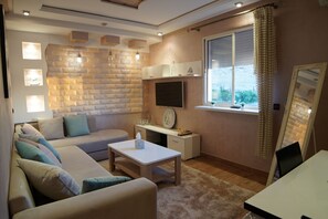 Ein modernes Wohnzimmer mit einer Couch, einem Couchtisch, einem Fernseher und einem Fenster mit Vorhängen.