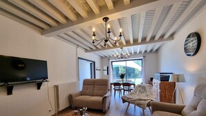 Sala de estar con televisor, sofá, sillón, mesa de comedor, candelabro y un reloj en la pared.