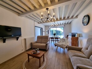 Ein Wohnzimmer mit Fernseher, Sofa, Sessel, Esstisch, einer Kristallleuchtre und einer Wanduhr.