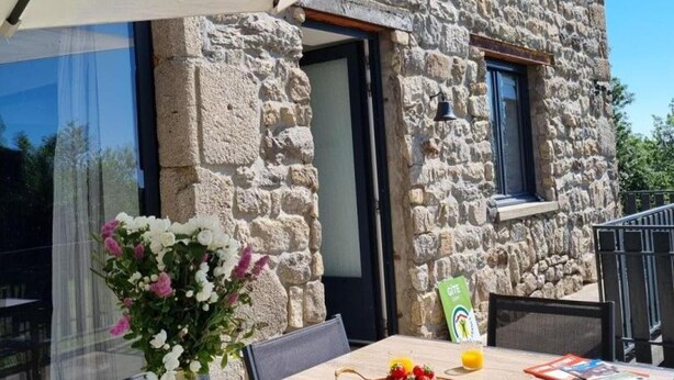 Un edificio de piedra con una mesa de comedor, sillas, un jarrón de flores y una cesta de fruta.
