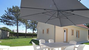 En terrasse med et bord og stole, en stor parasol og et hus i baggrunden.