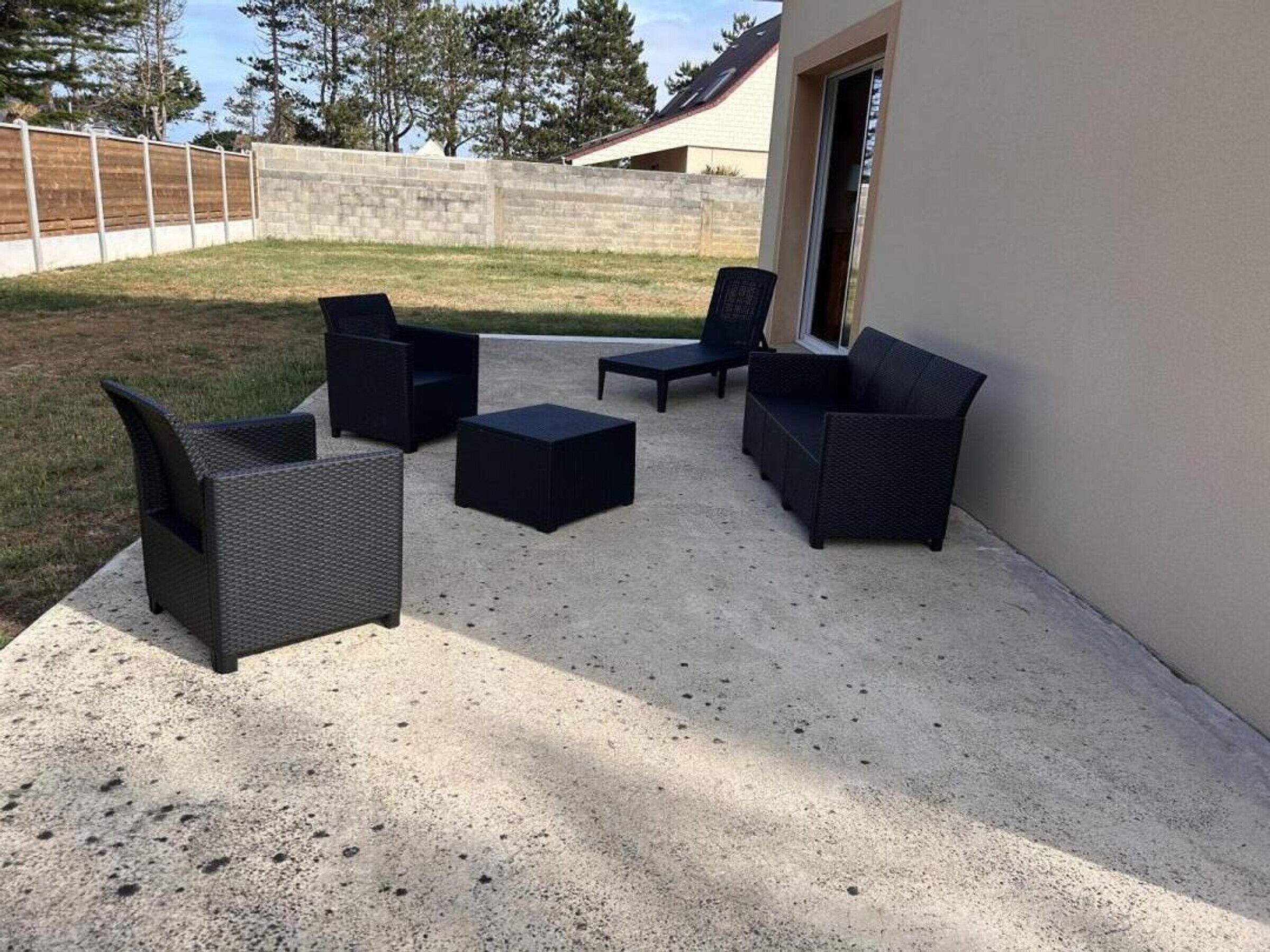 An outdoor patio with dark wicker furniture, a concrete floor, and a view of a house and trees in the background.