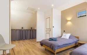 Ein Schlafzimmer mit Bett, Sessel, kleinem Tisch, Wandleuchte und einer Tür zu einem Badezimmer.
