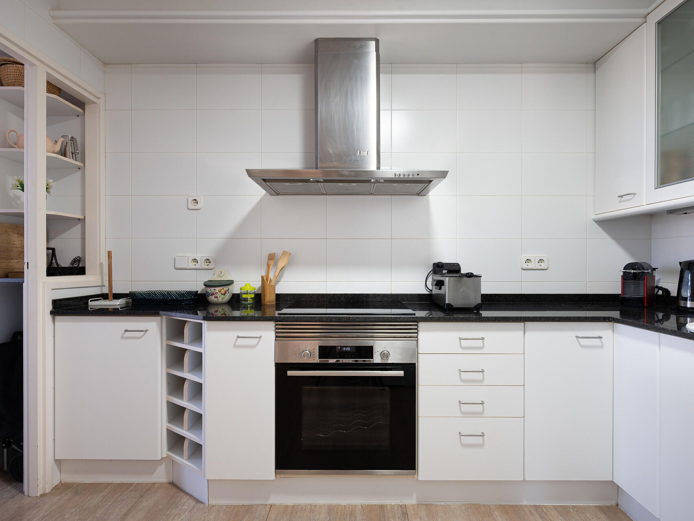 Een moderne keuken met witte kastjes, een roestvrijstalen afzuigkap, een inbouwoven en een zwart aanrecht.