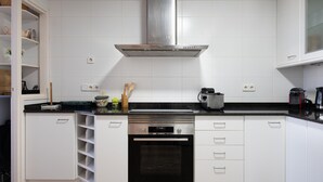 Una cocina moderna con armarios blancos, una campana extractora de acero inoxidable, horno empotrado y encimera negra.