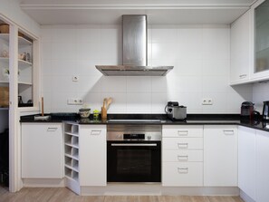 A modern kitchen with white cabinets, a stainless steel range hood, a built-in oven, and a black countertop. - Bright apartment, sea view - 6 guests (Torredembarra)