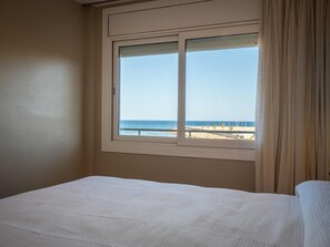 Ein Zimmer mit einem Bett, einem Fenster mit Blick auf den Strand und einem Vorhang.