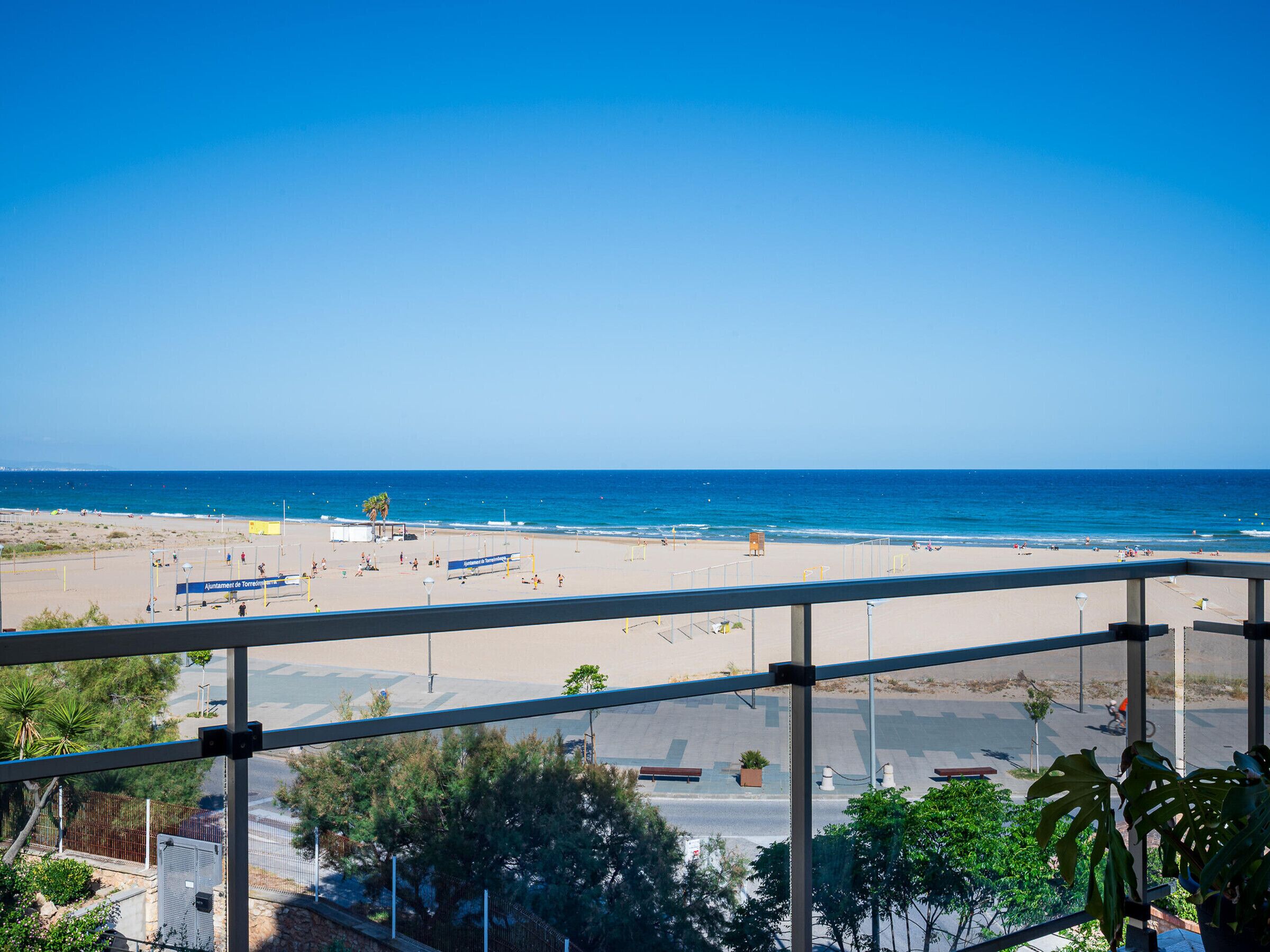 Uitzicht op een strand vanaf een balkon, met een heldere lucht, een zandstrand en enkele mensen in de verte.
