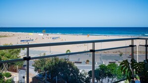 Vista a la playa desde un balcón, cielo despejado, arena y algunas personas a lo lejos.